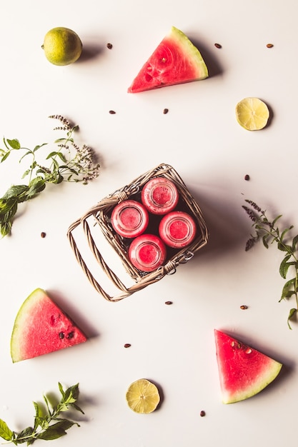 Délicieux boisson pastèque en bouteille d'été dans un panier et des tranches de fruits frais sur fond blanc