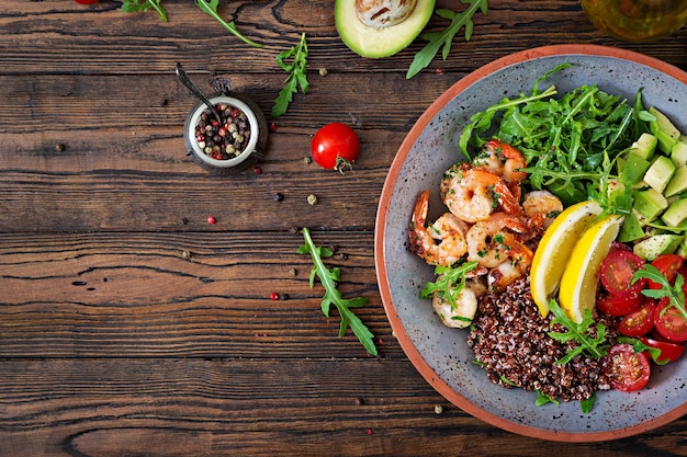 Délicieux bol de Bouddha sain avec crevettes, tomate, avocat, quinoa, citron et roquette sur la table en bois. Nourriture saine. Vue de dessus. Mise à plat.