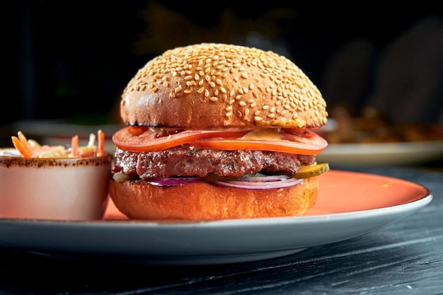 Délicieux burger au bœuf, tomates, oignons et sauce jaune, servi dans une assiette rouge avec salade de choux. restauration rapide américaine