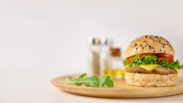 Délicieux burger de boeuf avec du fromage et des légumes frais sur une plaque en bois sur un tableau blanc