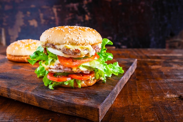 délicieux burger fait maison avec de la laitue, du fromage, de l&#39;oignon et des tomates sur une planche de bois rustique