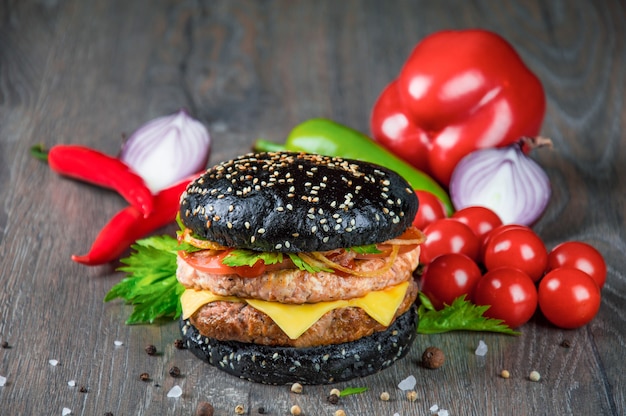 Photo délicieux burger noir juteux avec tomates fraîches, poivrons et herbes