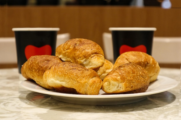 Photo délicieux café du matin pour deux petits pains frais sur fond de gobelets en papier sur une table dans un café en gros plan