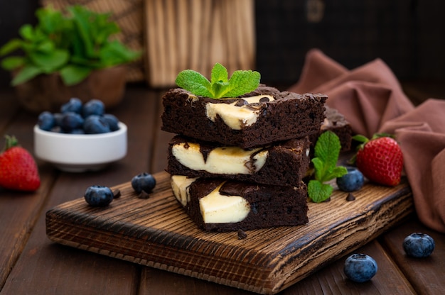 Délicieux cheesecake au brownie au chocolat avec des baies fraîches et de la menthe sur une planche de bois