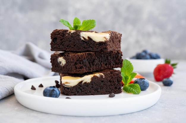 Délicieux cheesecake au brownie au chocolat avec des baies fraîches et de la menthe sur une plaque blanche