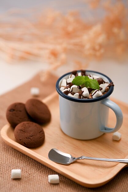 Délicieux chocolat noir malté avec de minuscules guimauves sur une assiette en bois avec des biscuits au chocolat noir