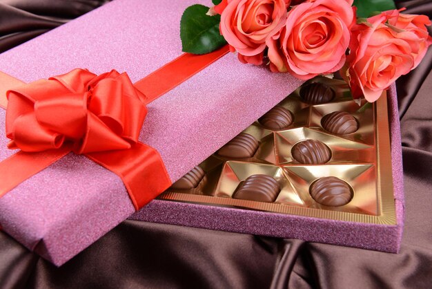 De délicieux chocolats en boîte avec des fleurs sur fond marron