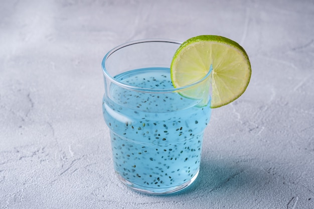 Délicieux cocktail de couleur bleue avec des graines de chia au basilic et une tranche de citron vert en verre