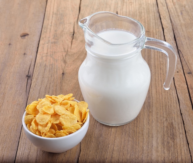 Délicieux cornflakes dans un bol blanc et un verre de lait sur une table en bois