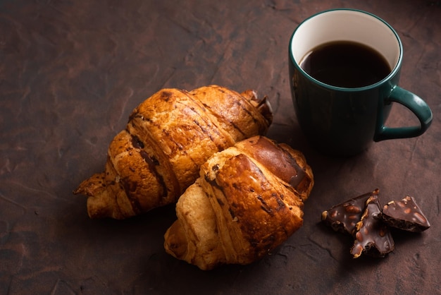 Délicieux croissants croustillants au chocolat café chaud dans la tasse bleue sur la plaque sur la table sombre Petit-déjeuner savoureux