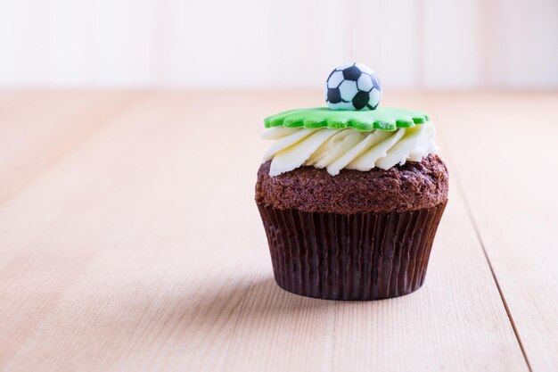 Délicieux cupcake avec icône de balle dessus sur un bureau en bois