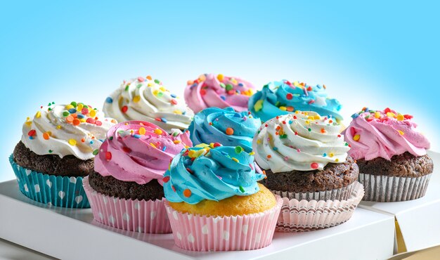 Délicieux cupcakes festifs dans une boîte de livraison pour la fête, divers cupcakes à la crème rose blanche et bleue sur fond bleu. Espace de copie