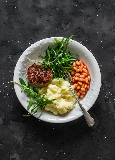 Délicieux déjeuner escalopes de dinde purée de pommes de terre haricots sauce tomate et salade de roquette sur fond sombre vue de dessus