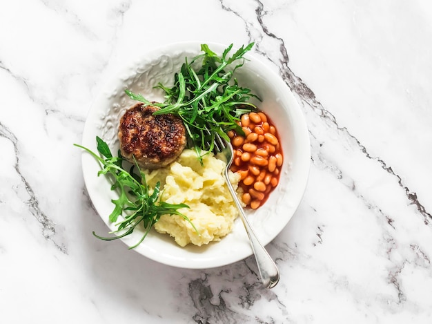 Délicieux déjeuner escalopes de poulet purée de pommes de terre haricots sauce tomate et salade de roquette sur fond clair vue de dessus