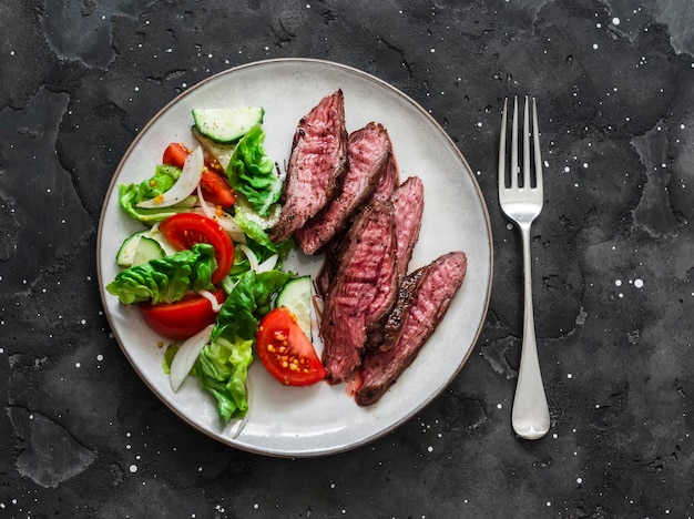 Délicieux déjeuner laitue concombre salade de tomates et steak de boeuf sur fond sombre vue de dessus