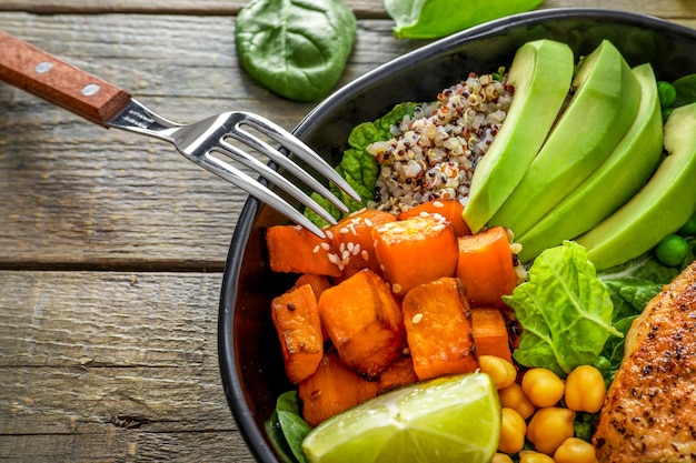 Délicieux déjeuner avec quinoa, avocat, patate douce, poulet frit et assaisonnement sur fond en bois.