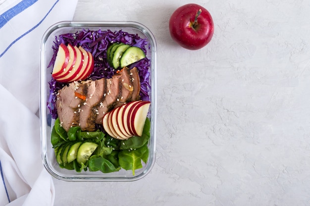 Délicieux déjeuner sain de légumes et de dinde au four. Salade de chou rouge, épinards, pommes, concombres frais avec viande diététique dans une boîte à lunch en verre. Contexte