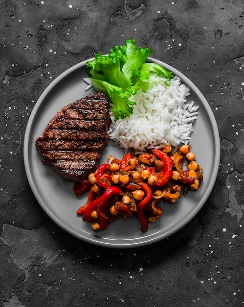 Délicieux déjeuner steak de riz grillé et ragoût de pois chiches au poivre d'aubergines rôties sur une vue de dessus de fond sombre