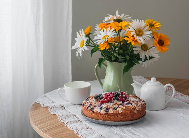 Délicieux dessert d'été tarte aux baies un bouquet de marguerites dans un pot sur une table ronde dans un salon confortable