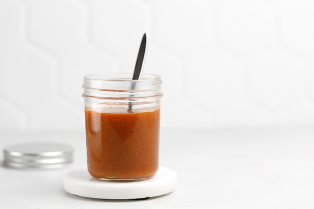 Délicieux dessert sauce caramel en pot avec cuillère sur fond blanc Caramel dans un bocal en verre