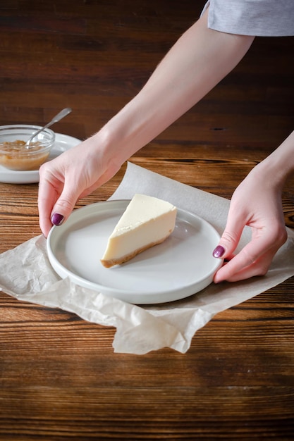 Délicieux dessert sucré gâteau au fromage classique New York sur fond rustique en bois Mains de femme servant une tranche de gâteau savoureux sur une assiette en céramique avec fourchette à dessert et confiture de pomme