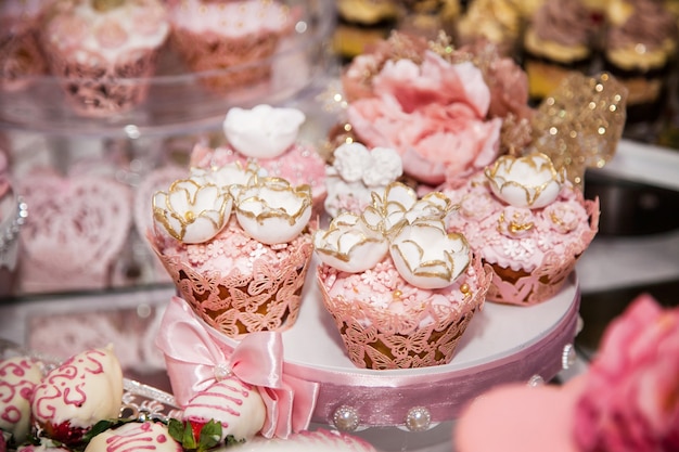 Délicieux desserts au bar à bonbons de mariage dans l'espace buffet : muffins décorés d'anges, boutons de rose en sucre et teinture d'or