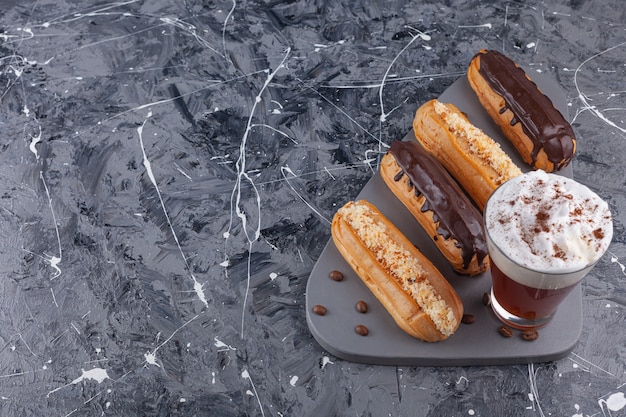 Délicieux éclairs de chocolat et de vanille et avec une tasse de café sur une planche à découper noire.