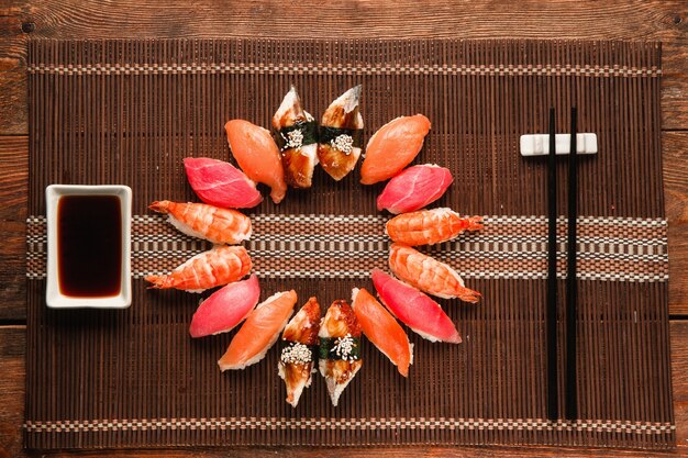 Un délicieux ensemble appétissant de sushis nigiri colorés a servi de cercle sur un tapis de paille marron, à plat. Fruits de mer traditionnels japonais.