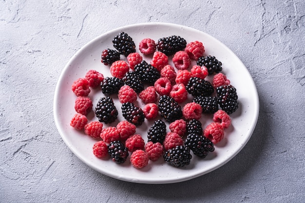 Délicieux fruits mûrs de framboise et de mûre dans la plaque, des aliments sains fruits sur table en béton en pierre, vue d'angle