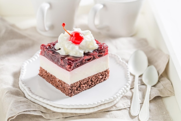 Délicieux gâteau aux cerises en gelée sur une assiette blanche avec de la crème