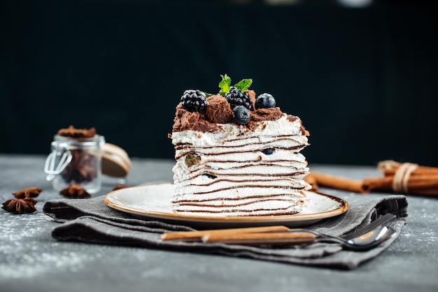 Délicieux gâteau aux crêpes au chocolat sucré avec de la crème au beurre et des baies sur une plaque sur un fond gris