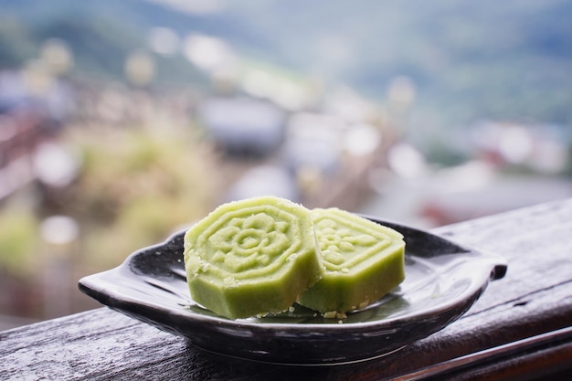 Délicieux gâteau aux haricots mungo verts avec une assiette de thé noir sur une balustrade en bois d'un salon de thé à Taïwan avec un beau paysage en arrière-plan de près