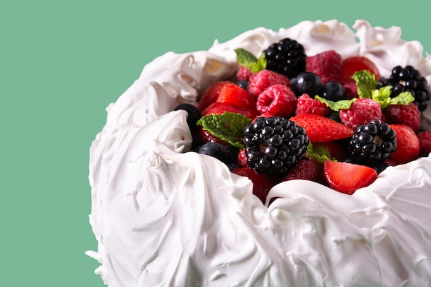 Délicieux gâteau Pavlova avec meringue surmontée et baies fraîches sur fond vert