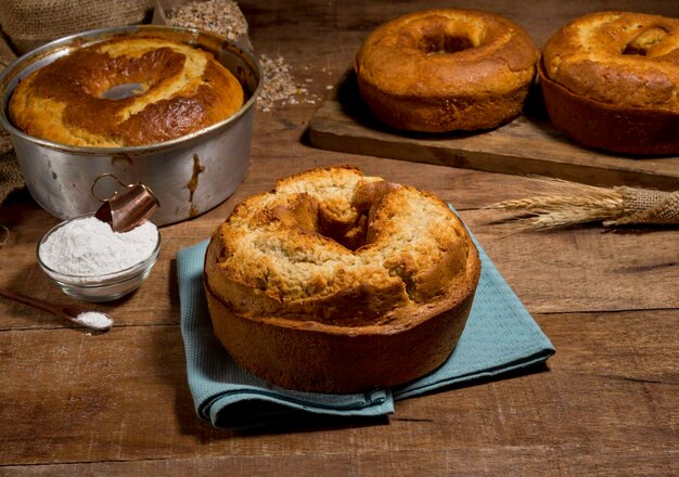 Délicieux gâteau traditionnel sur tissu bleu avec d'autres gâteaux et éléments de recette en arrière-plan, sur bois rustique.