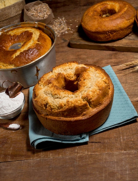 Délicieux gâteau traditionnel sur tissu bleu avec d'autres gâteaux et éléments de recette en arrière-plan, sur bois rustique.