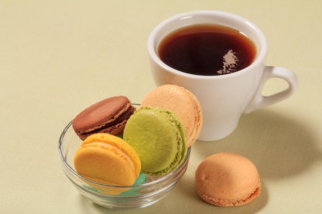 Délicieux gâteaux de macarons de couleur différente dans un bol en verre et une tasse de café sur fond beige.