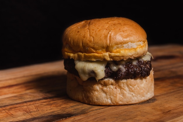 Délicieux hamburger avec beaucoup de fromage sur une table en bois sur fond noir.