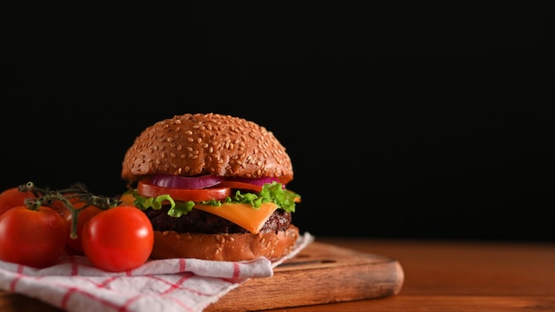 Délicieux hamburger de boeuf grillé servi sur un plateau en bois sur la table avec serviette au restaurant avec mur noir