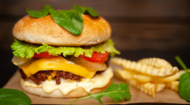 Délicieux hamburger fait maison avec du boeuf, de la laitue, du fromage, du concombre et des frites sur un fond de bois