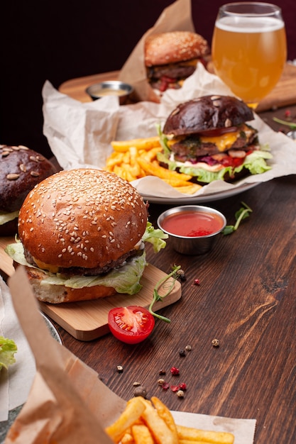 Délicieux hamburger frais avec laitue, fromage, oignon, tomate sur une planche de bois rustique sur fond marron. Frites également dans du papier ketchup, du ketchup et de la bière. Tir vertical.