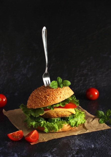 Délicieux hamburger frais avec tomates escalopes concombres fromage et basilic sur fond sombre avec une fourchette