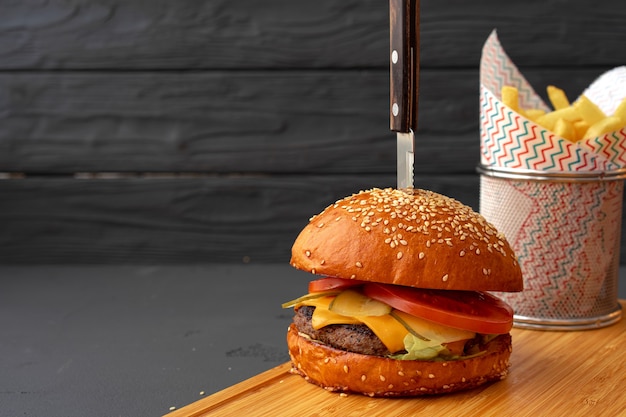 Délicieux hamburger et frites sur planche de bois sur fond noir, vue de face