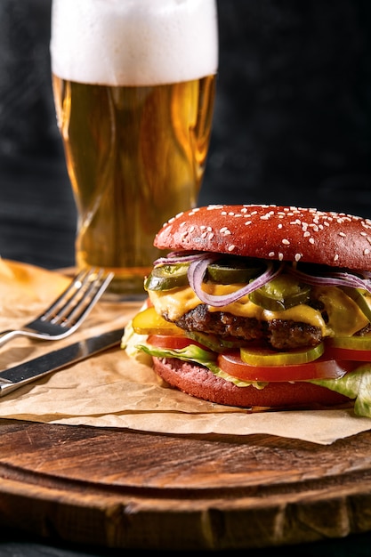 Délicieux hamburger noir épicé chaud avec du piment et un verre de bière sur une planche à découper sur une table en bois blanc