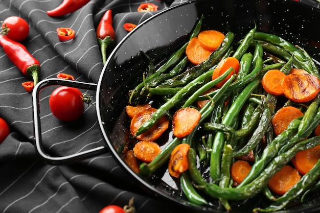 Délicieux haricots verts et tranches de carottes dans une poêle sur tissu noir