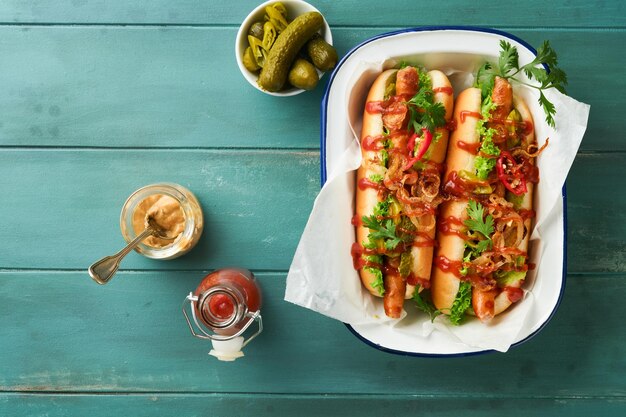Délicieux hot-dog grillé avec des concombres marinés, des piments, des oignons caramélisés, du ketchup et de la moutarde dans du papier kraft sur un vieux fond en bois bleu. Hot-dog américain fait maison pour la célébration du 4 juillet.