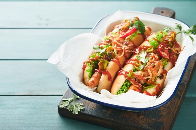 Délicieux hot-dog grillé avec des concombres marinés, des piments, des oignons caramélisés, du ketchup et de la moutarde dans du papier kraft sur un vieux fond en bois bleu. Hot-dog américain fait maison pour la célébration du 4 juillet.