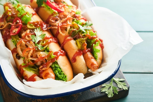 Délicieux hot-dog grillé avec des concombres marinés, des piments, des oignons caramélisés, du ketchup et de la moutarde dans du papier kraft sur un vieux fond en bois bleu. Hot-dog américain fait maison pour la célébration du 4 juillet.