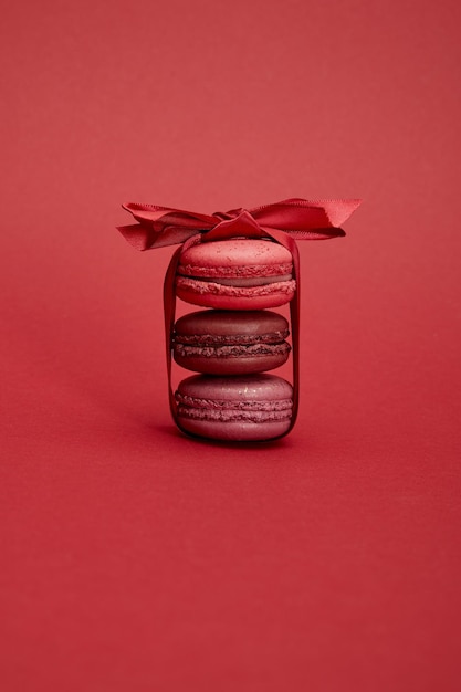 Délicieux macarons français colorés enveloppés dans un ruban avec un arc sur fond rouge