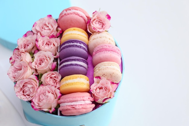 Délicieux macarons et roses en boîte sur fond clair