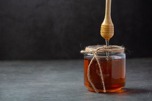 Délicieux miel avec louche de miel en bois sur une surface sombre